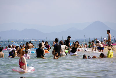 滋賀県湖西・近江舞子の雄松浜の突端辺りで湖水浴に興じる多くの人々と対岸背後い浮かぶ近江富士「三上山」