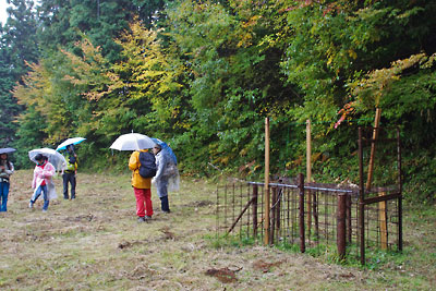 滋賀県北西・比良山塊西部支脈に抱かれた畑集落山際に現れた熊用の罠と、傘をさしつつ寛ぐ山会一行