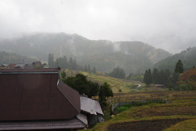 滋賀県北西・比良山塊西部支脈に抱かれた畑集落西部上方から見た、雨に煙る集落と棚田に紅葉の山