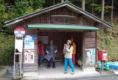 滋賀県北西・比良山塊西部支脈に抱かれた山間集落「畑」の木製停留所で雨に備える山会一行
