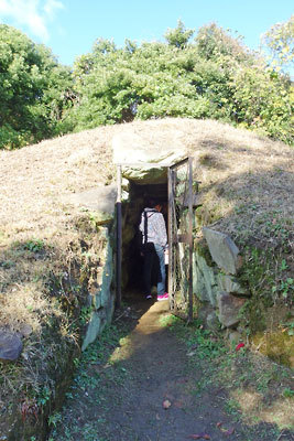 史跡大江山古墳群の円墳「14号墳」の石室口と、その奥にのぞく内部で説明を聞く見学者