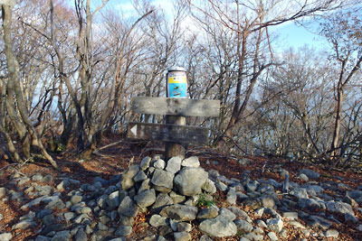 穏やかな平坦地と冬枯れの灌木に囲まれた標識が立つ、滋賀県西部・比良山脈北部の一峰「釈迦岳」山頂