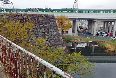 京都市街南部にある旧淀城の天守台石垣と内堀跡に、背後の高架を走る京阪電車