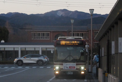 京都市街北部・国際会館駅前ターミナルに停車する鞍馬からのバスと夕暮空に立つ天狗杉山とその南面雪原