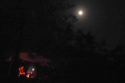 野営地の焚火上に昇る満月に近い月