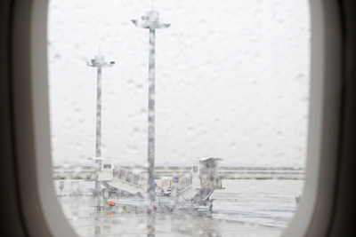降り出した雨に濡れる飛行機の窓と関西空港駐機場